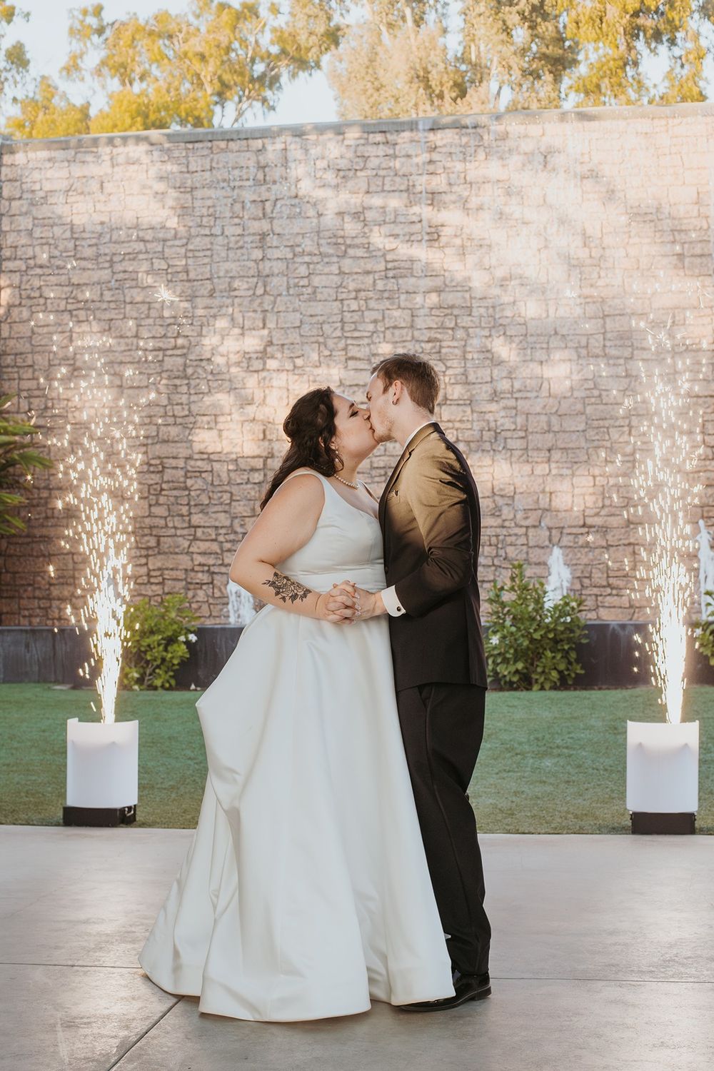 A couple shares their first dance outdoors with sparkler fountains glowing in front a stone wall at River Garden Weddings and Events..