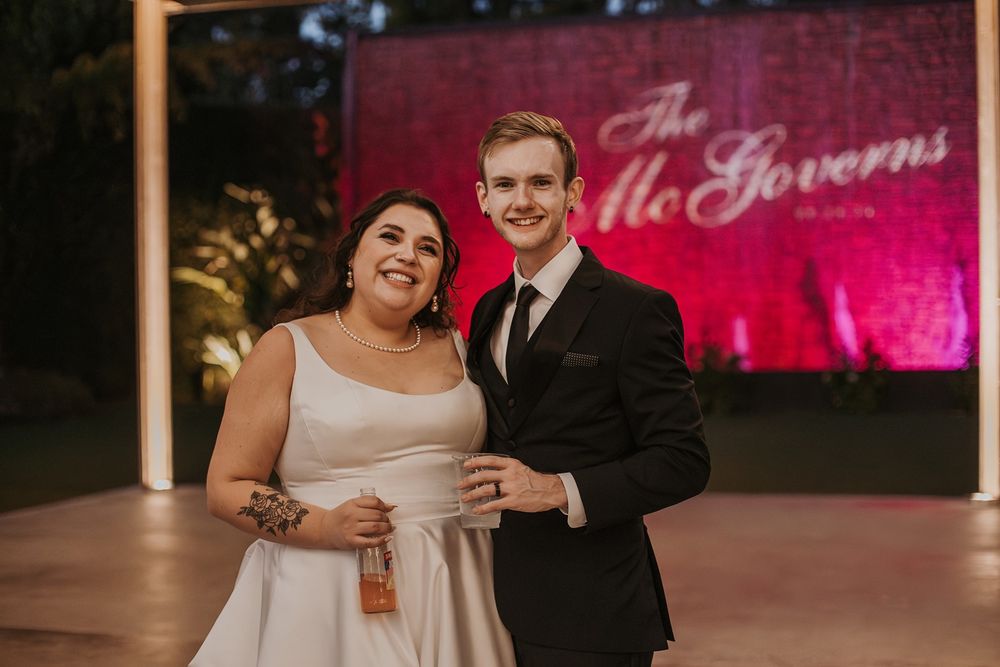 A couple shares a joyful moment on their wedding day with pink lighting in the background at River Garden Weddings and Events.
