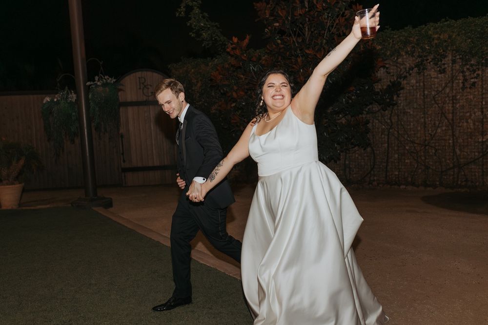 A couple runs together at night in an outdoor setting, with the bride's white dress flowing gracefully at River Garden Weddings and Events.