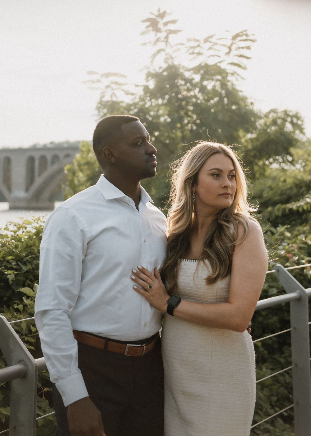 A couple poses against a railing during golden hour with water views.