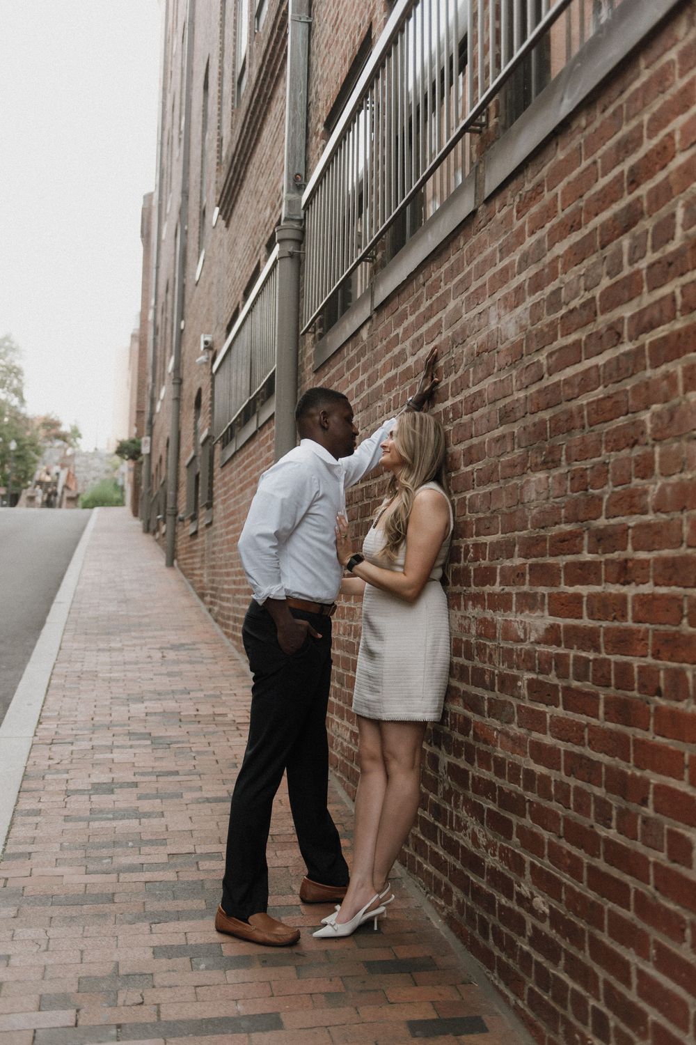 A romantic couple shares an intimate moment against a brick wall in an urban alleyway.