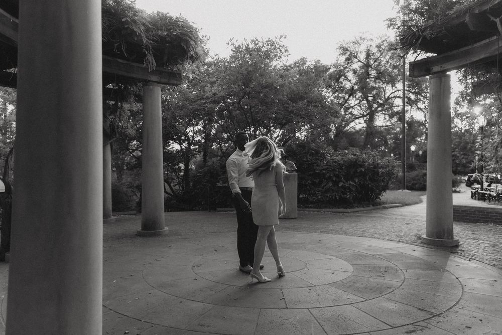 A couple shares an intimate moment under white pillars in a garden setting.