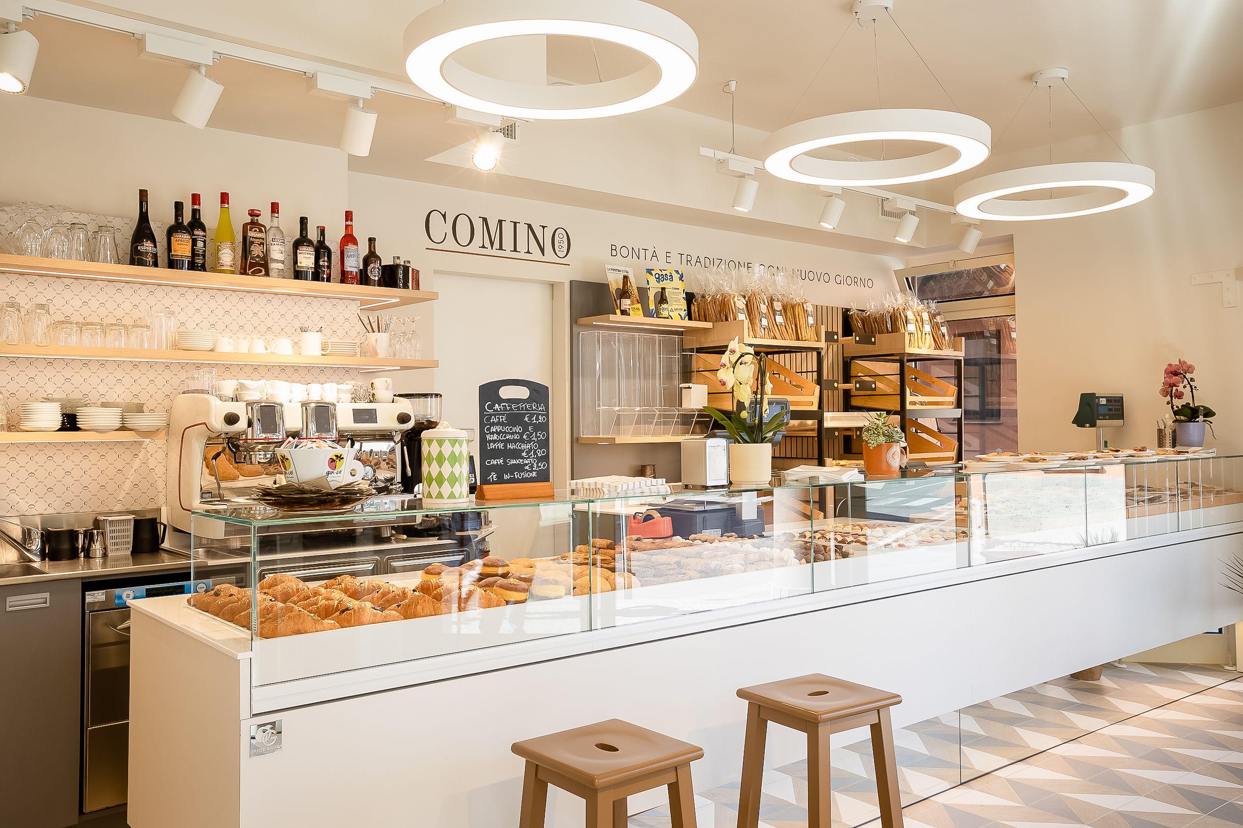 Modern bakery interior with white counters, circular pendant lights, and pastry displays showcasing fresh baked goods.