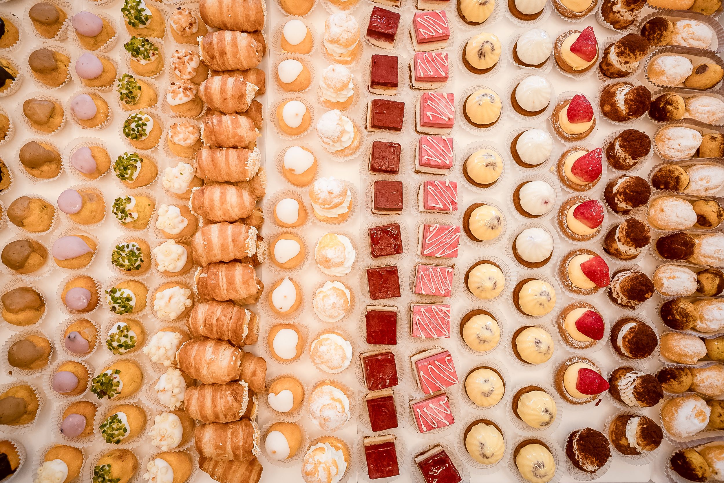 Colorful rows of assorted French macarons in pastel shades displayed in a bakery case.