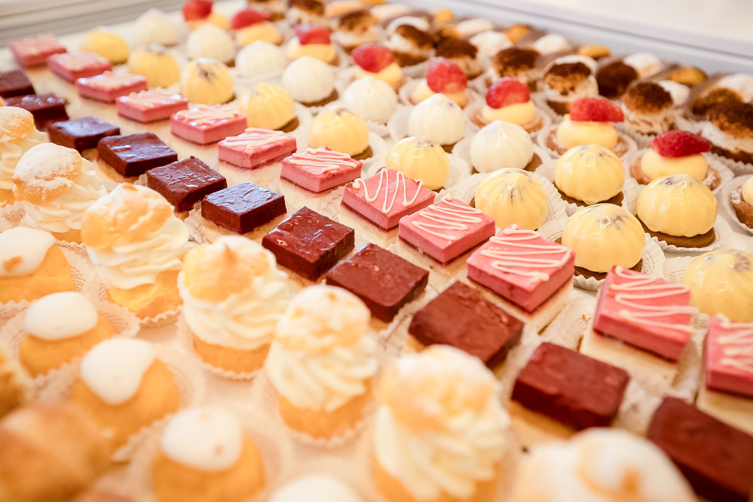 Rows of colorful French pastries and petit fours displayed on a catering table.