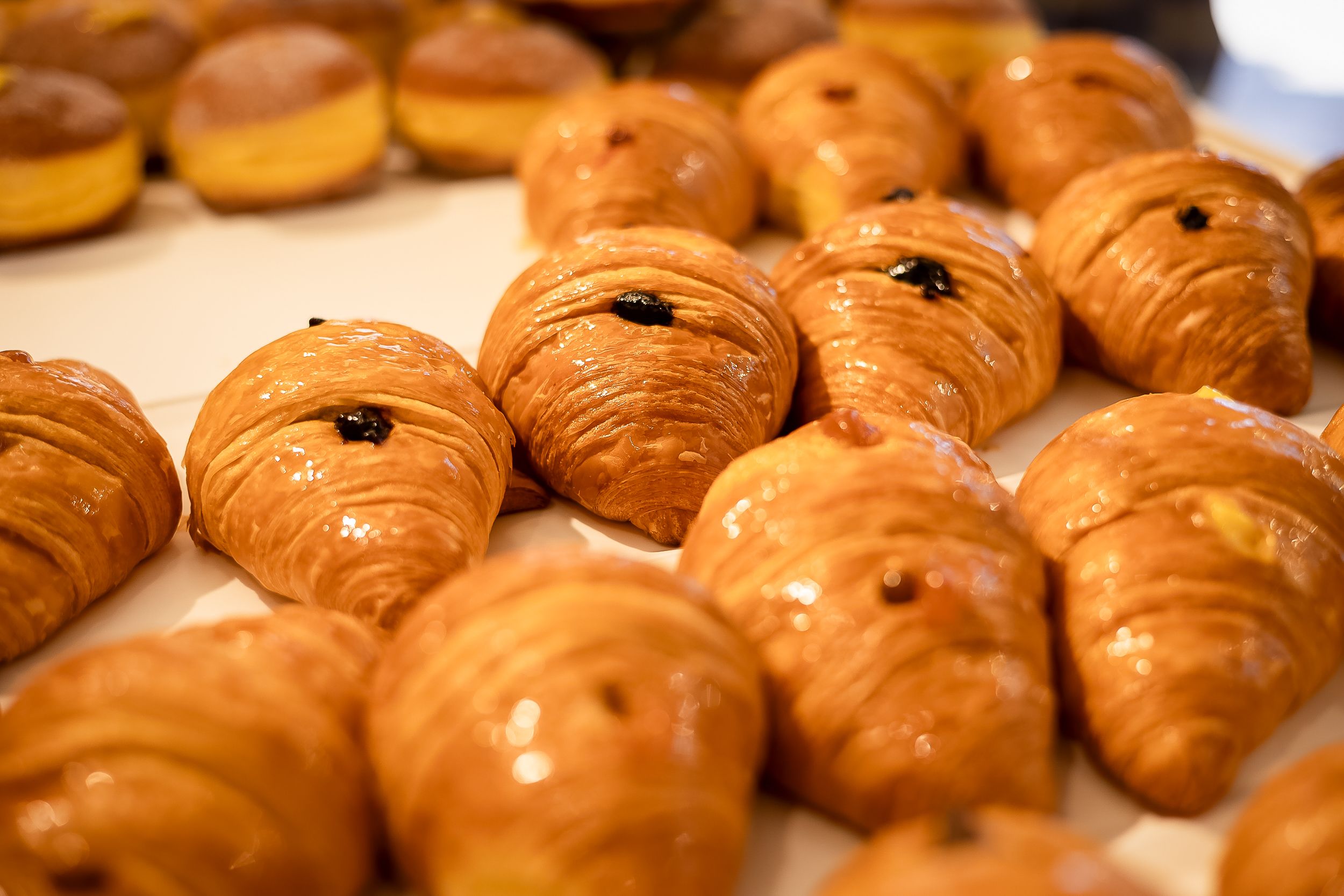 Freshly baked golden croissants arranged in neat rows on a display with a glossy, flaky exterior.