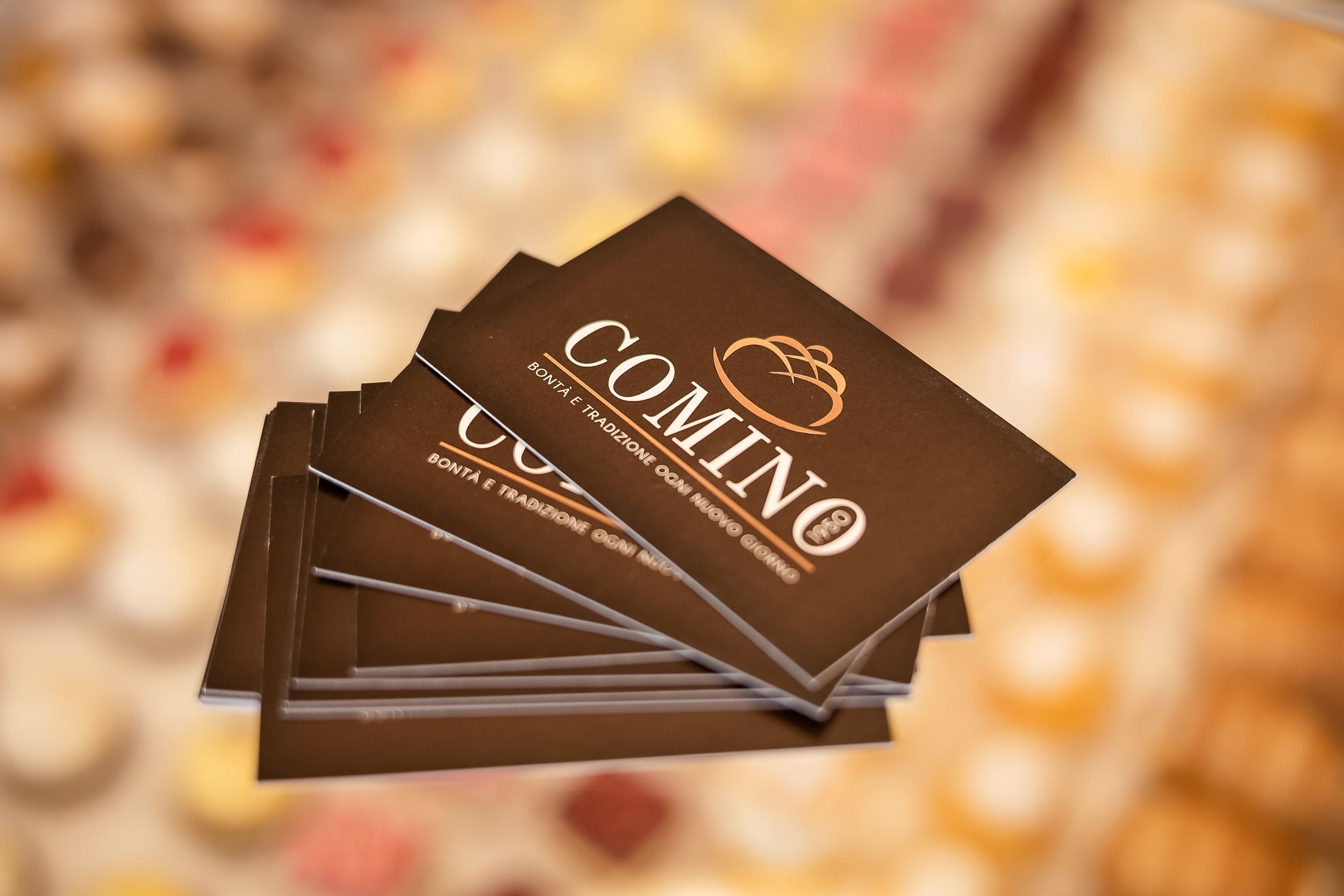 Stack of dark brown chocolate bars with gold lettering scattered on wooden surface with blurred background.