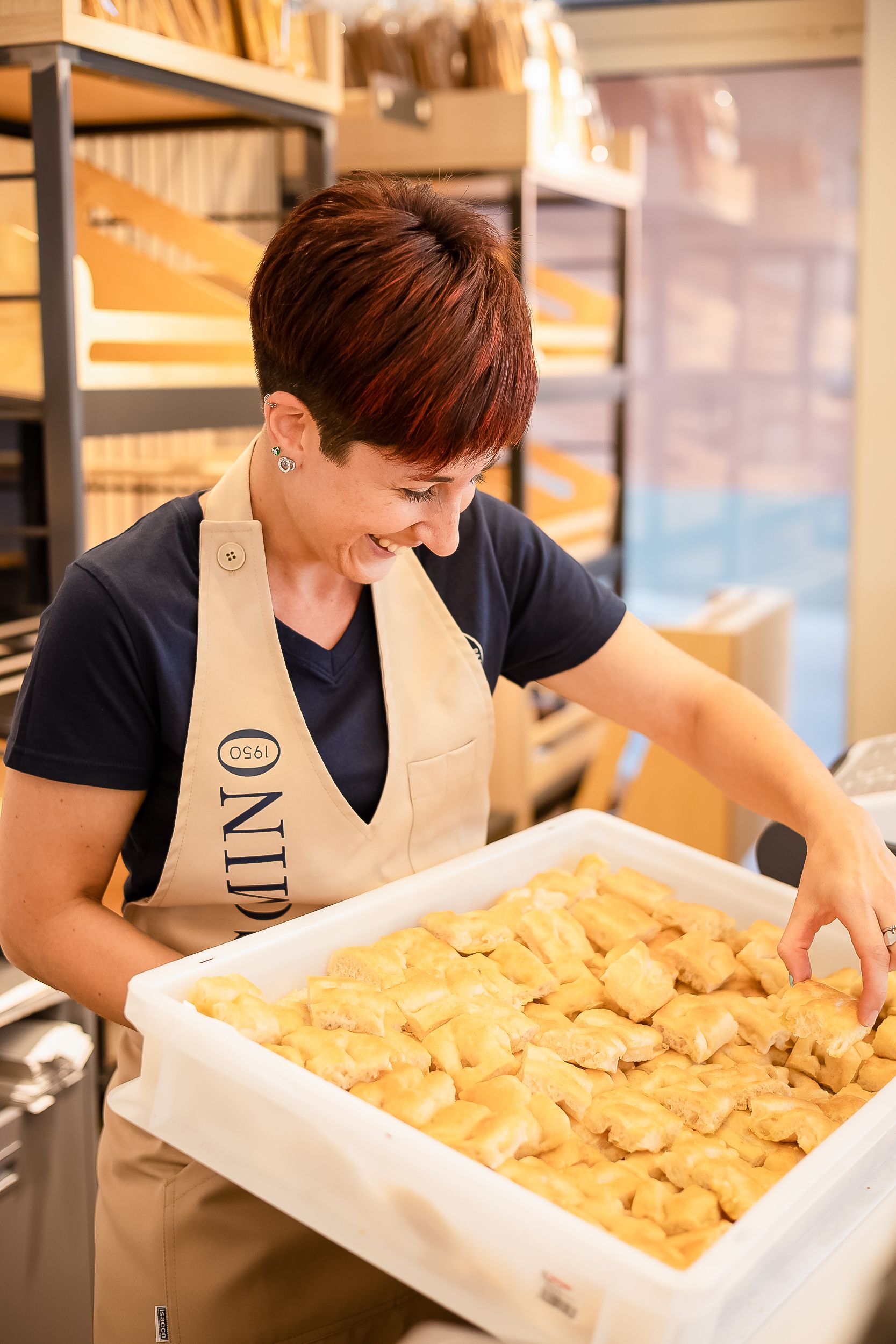Staff member in black shirt and beige apron arranges fresh handmade dumplings in a large white tray at a restaurant.