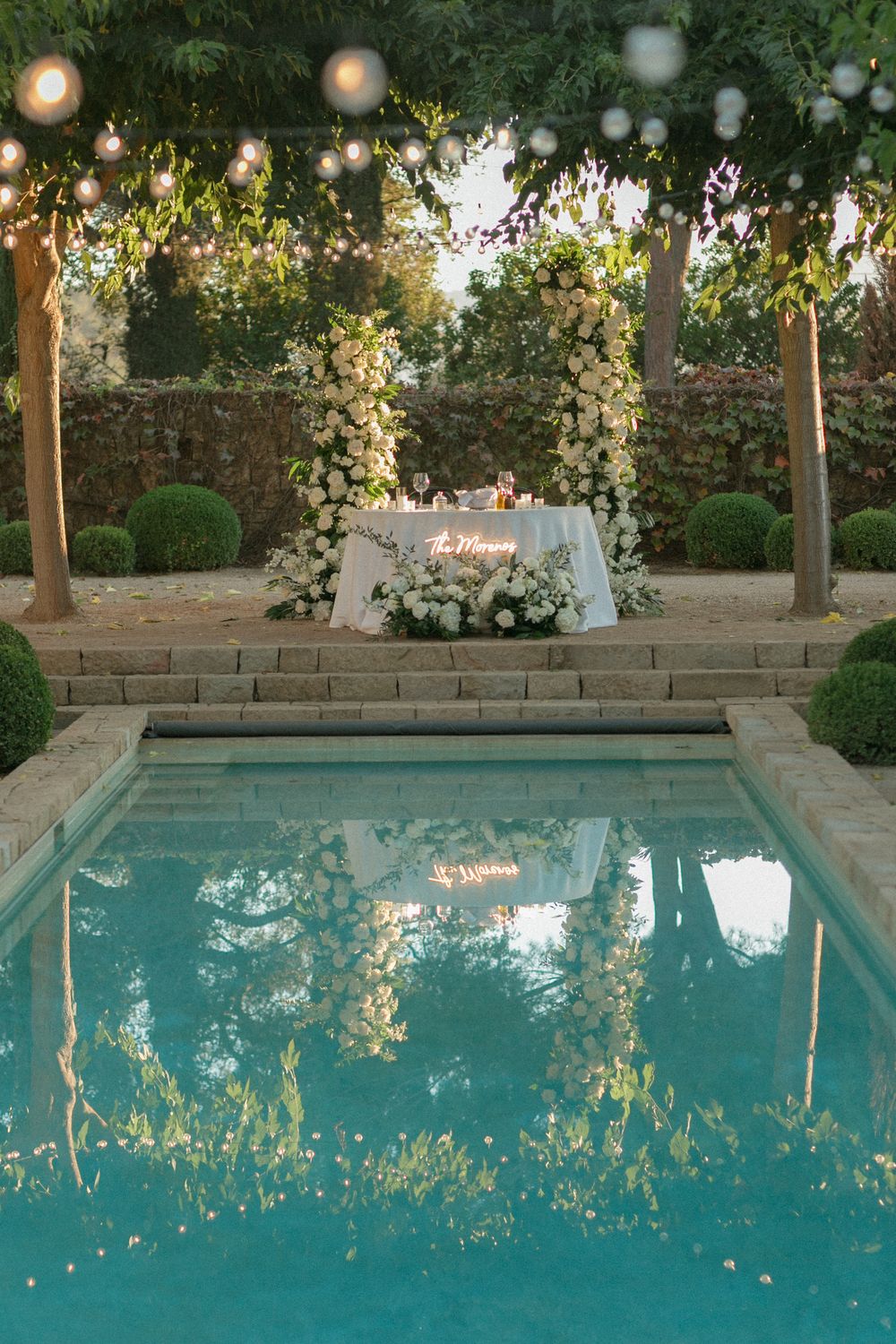 Elegant outdoor swimming pool with string lights and landscaping reflecting in crystal clear turquoise water at dusk.