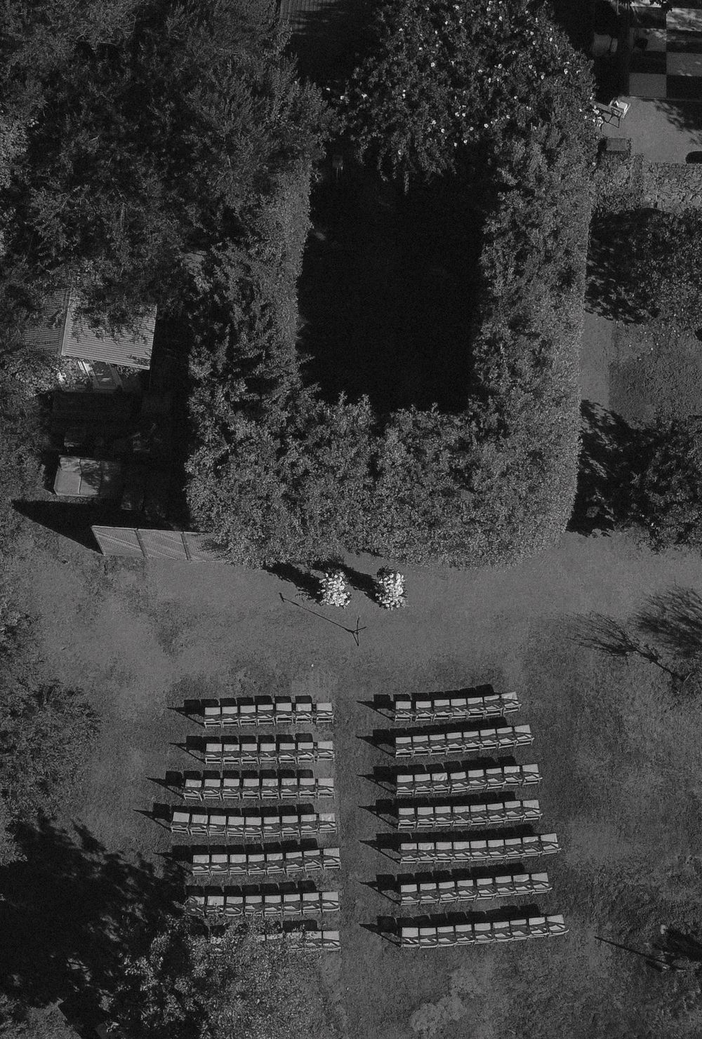 Aerial view of rows of empty white chairs arranged outdoors in a garden setting for an event.