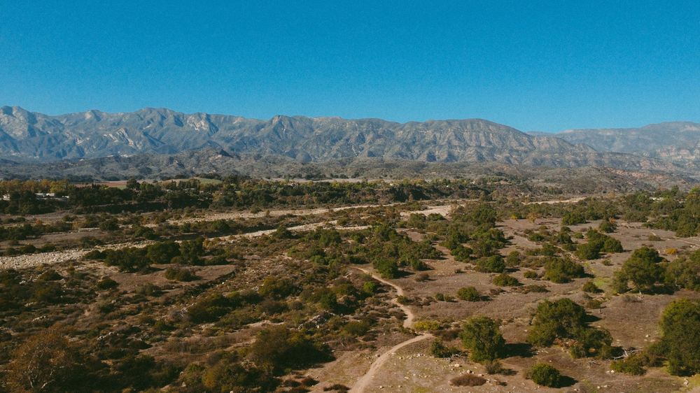 Panoramic desert landscape with rugged mountain ranges and arid terrain stretching to the horizon under clear blue skies.