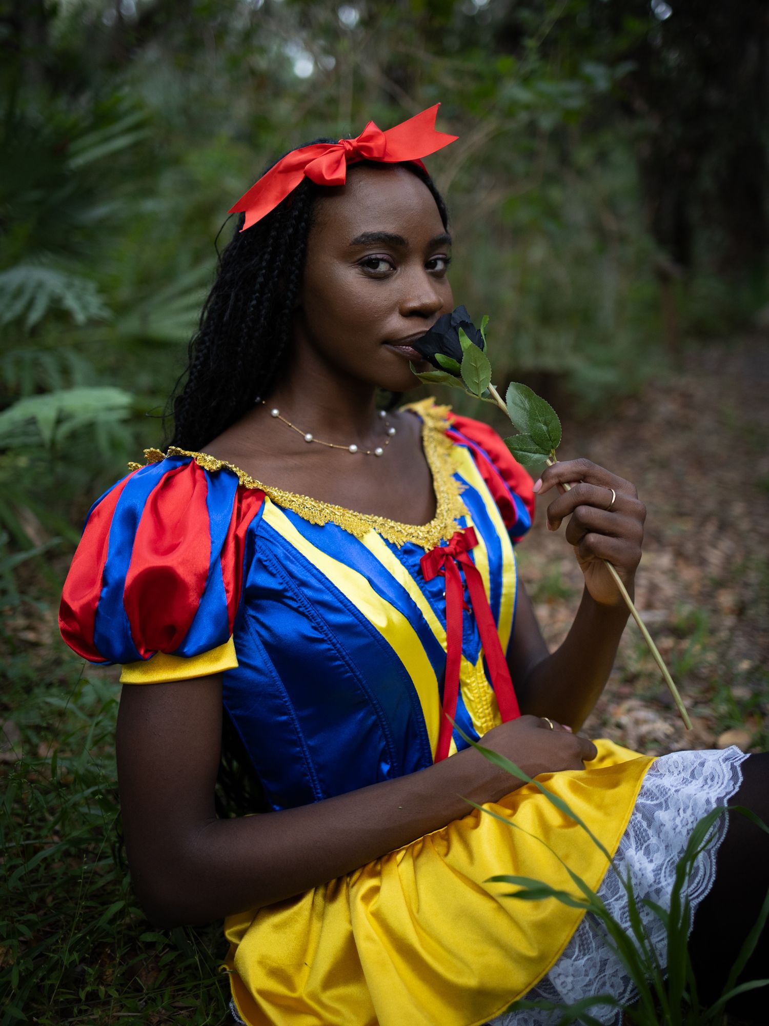 A person in a Snow White inspired costume poses gracefully in a woodland setting with natural lighting.