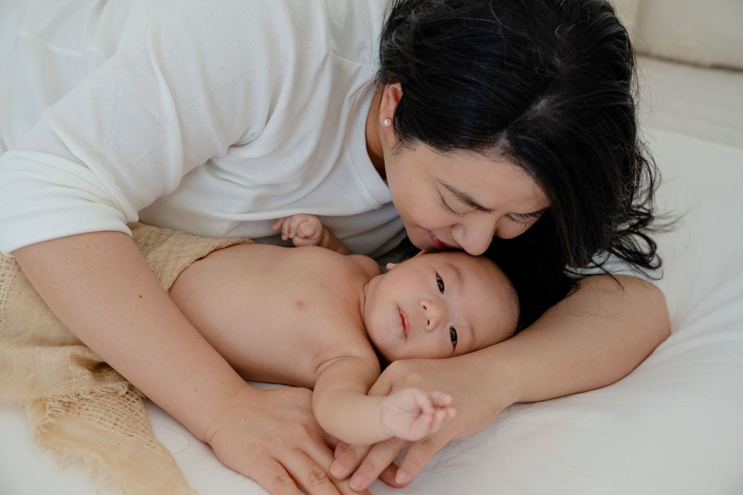Mother and baby lying together on bed sharing tender intimate bonding moments.