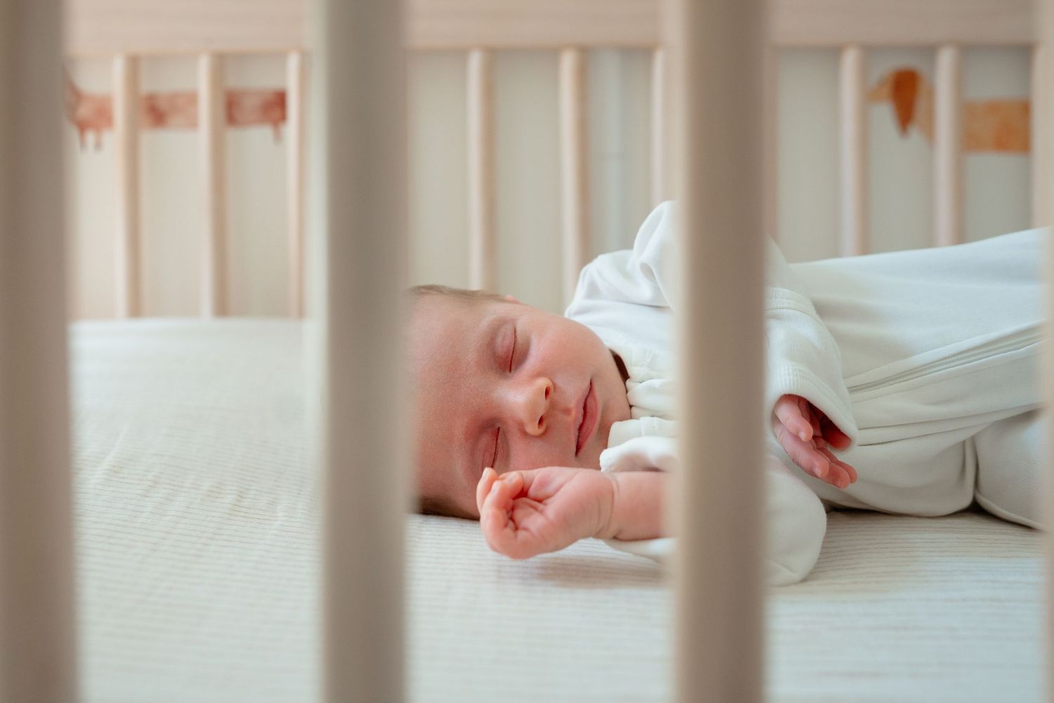 A sleeping baby rests peacefully in a white crib with slat railings.