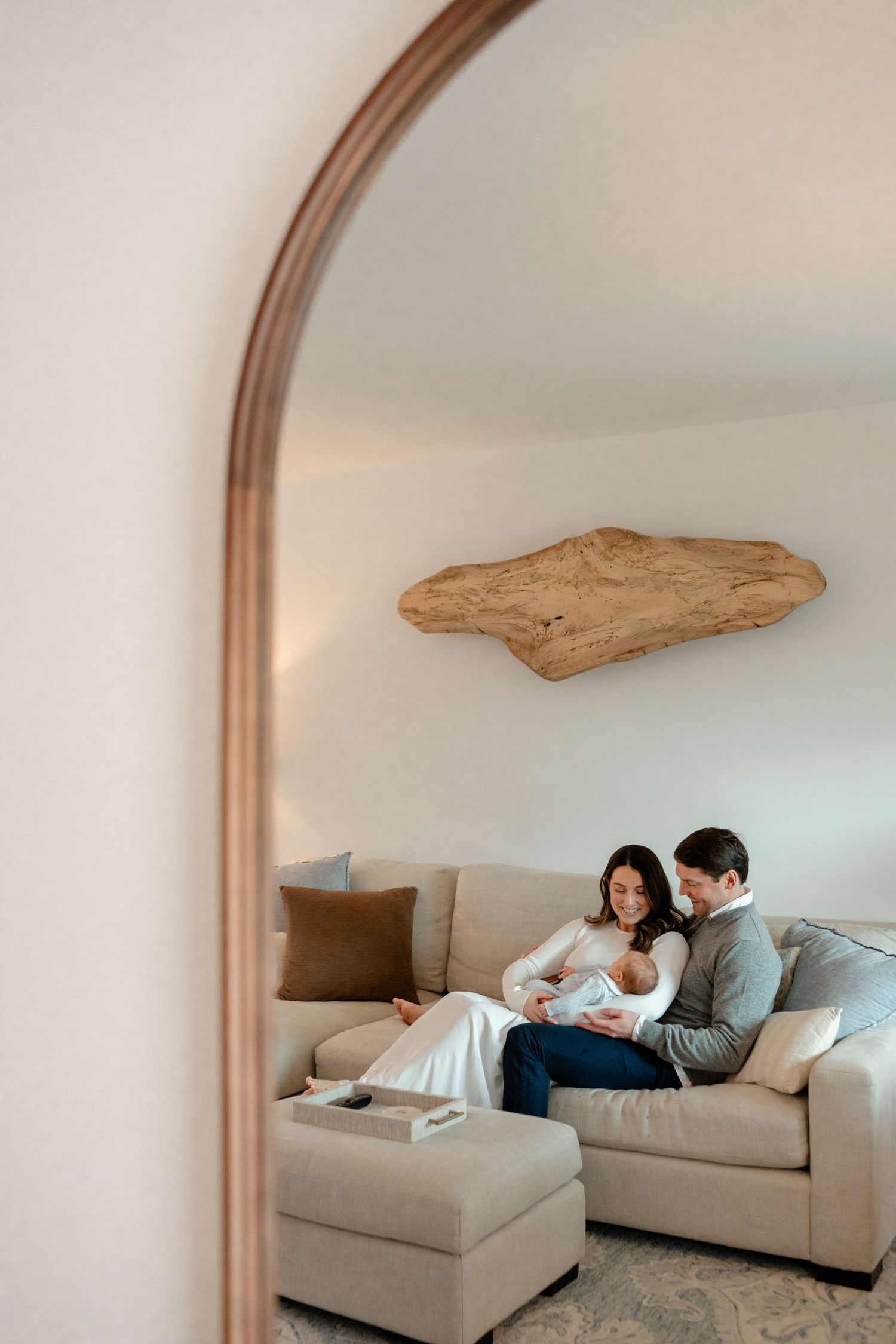 A couple lounges together on a light gray sectional sofa beneath a curved archway in a minimalist white room.