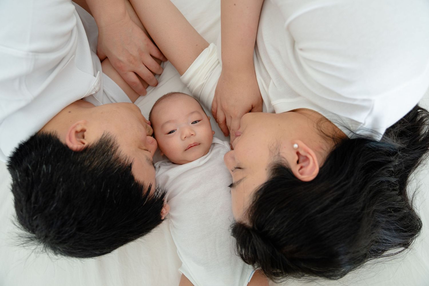 Four sequential photos showing a tender moment between a parent and baby lying together on white bedding.