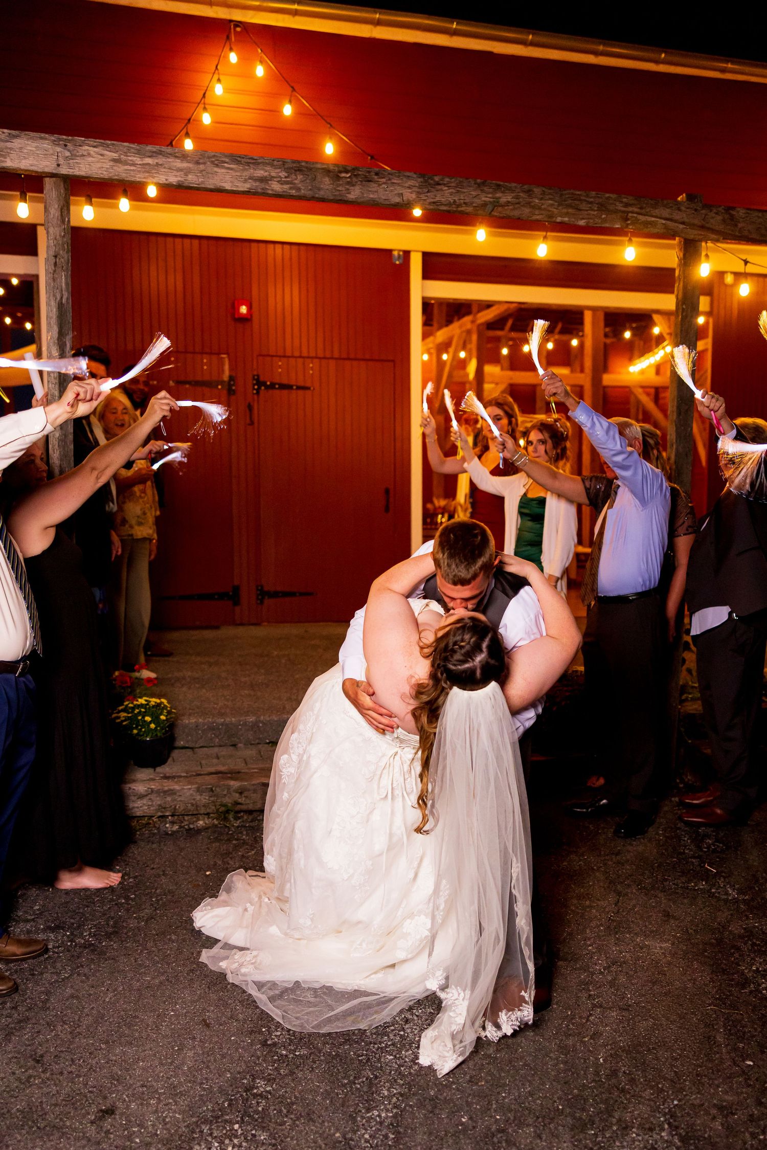 frederick maryland wedding photogCouple shares romantic dip kiss at wedding reception while guests cheer with sparklers under string lights.
