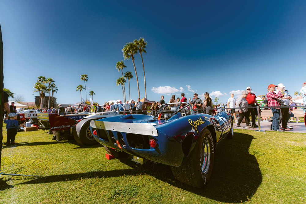 Vintage sports cars on display at an outdoor car show with palm trees and blue sky in the background.