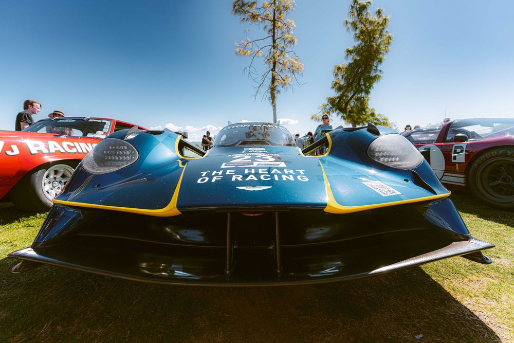 A collection of vintage race cars parked in a row at an outdoor motorsports event under blue skies.