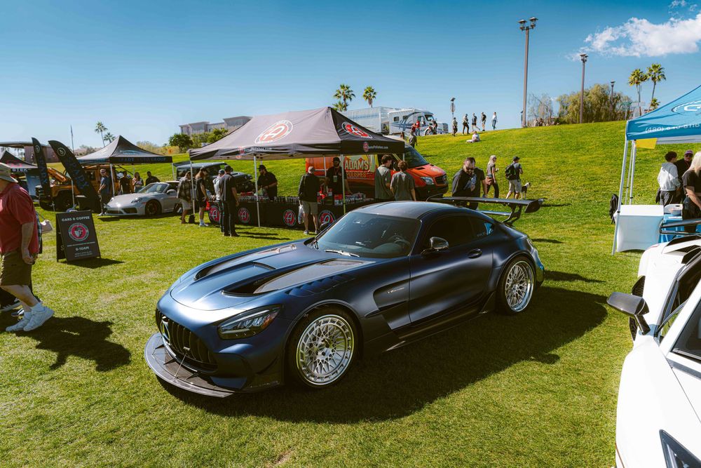 A sleek black Mercedes-AMG GT sports car with custom wheels displayed on grass at an outdoor car show event.