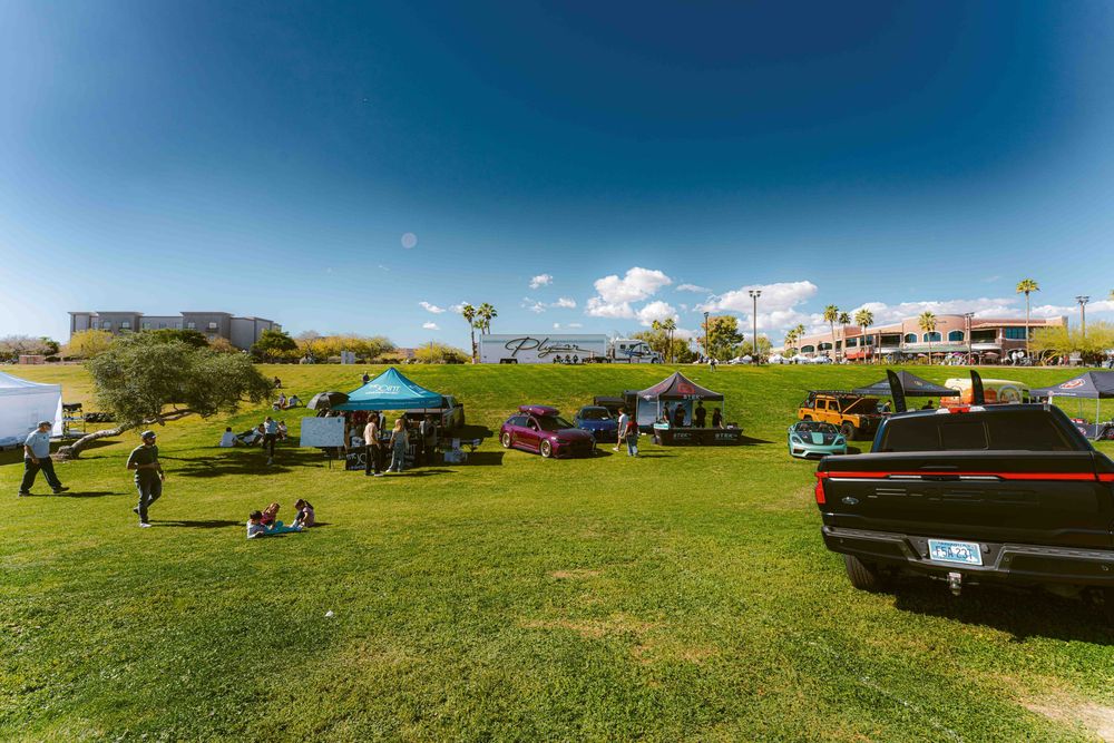 A panoramic view of classic cars displayed on a grassy hill against a bright blue sky on a sunny day.