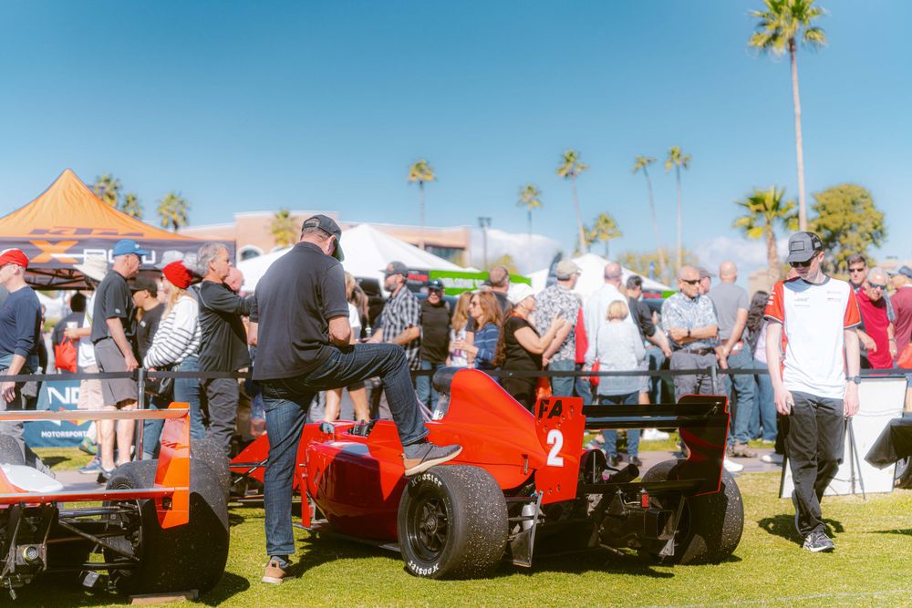A row of vintage red tractors on display at an outdoor farm equipment show with palm trees in the background.