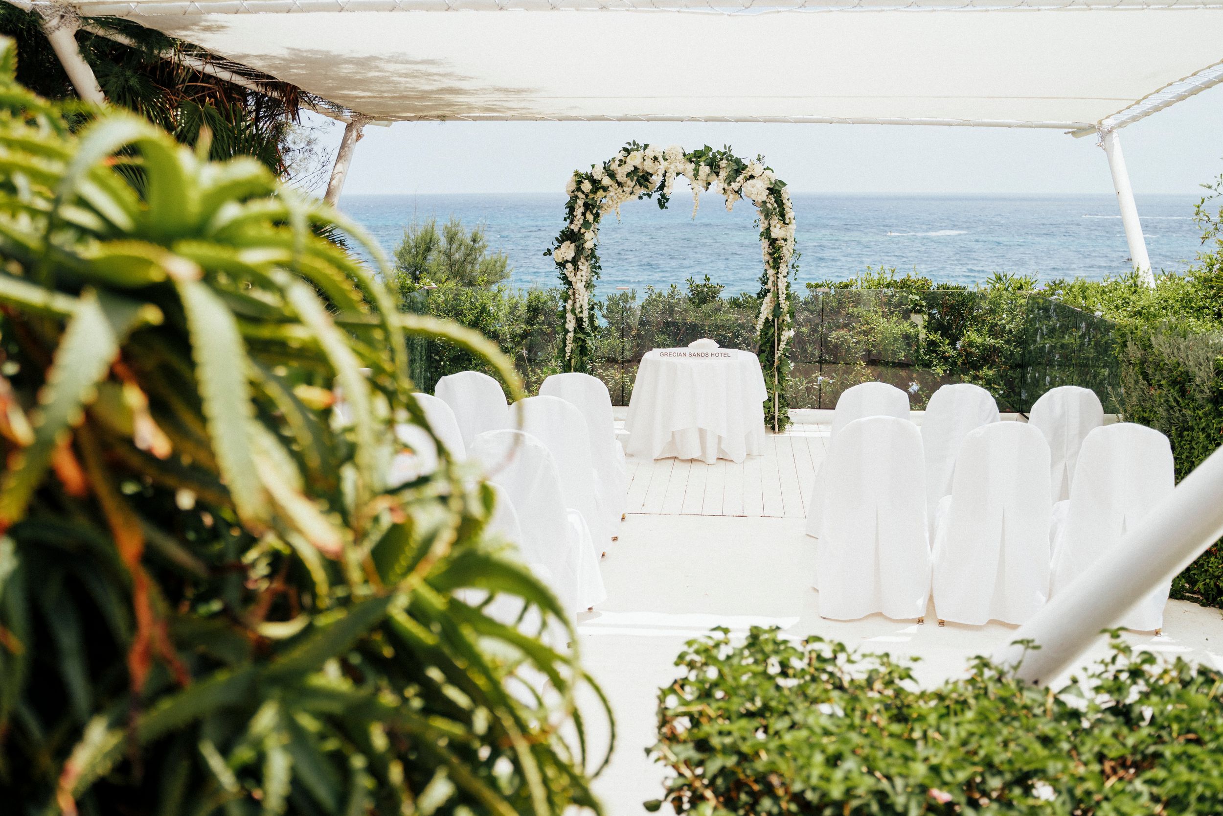 White chairs arranged for an outdoor wedding ceremony under a floral arch with mountain views in the background.