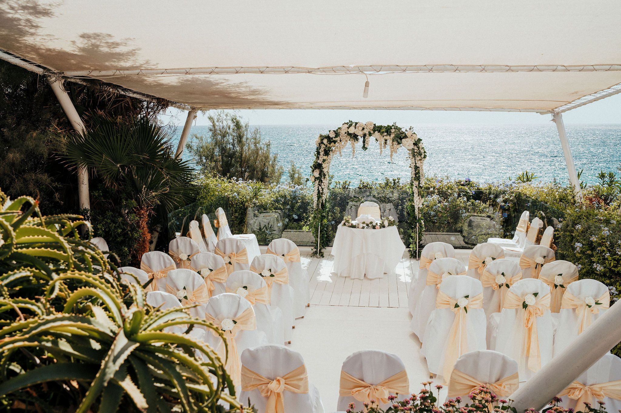 A stunning outdoor wedding reception setup with white tablescapes and floral arrangements overlooking a scenic ocean view.