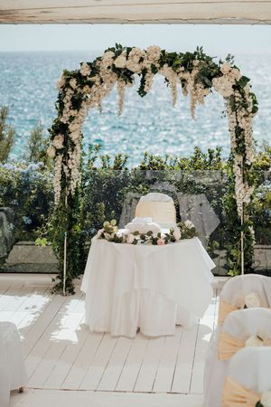 Beautiful floral wedding arch with white flowers and greenery overlooking the ocean at an elegant outdoor ceremony setup.
