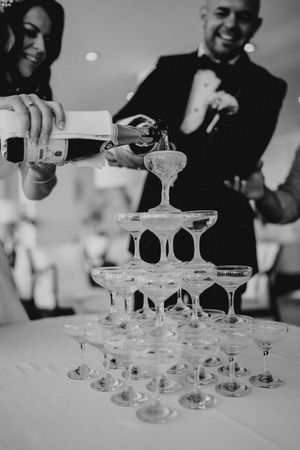 Black and white photo series showing champagne being poured into a tower of stacked coupe glasses at an elegant event.