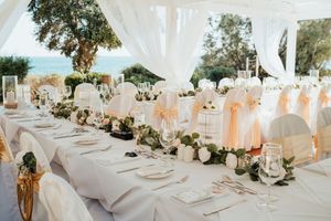 Elegant outdoor wedding reception table setting with white linens, floral centerpieces and flowing sheer tent draping.