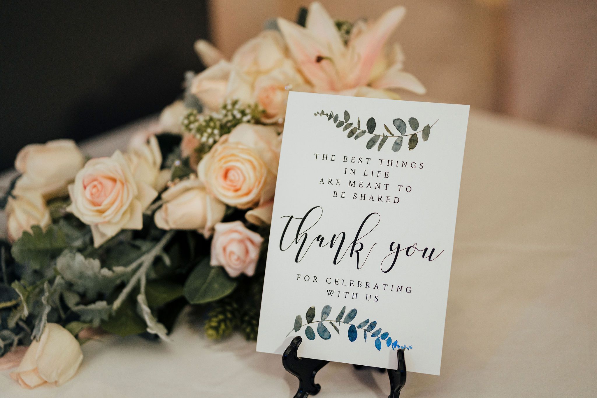Elegant wedding details with blush pink roses, calligraphy thank you cards, and delicate greenery arrangements on a table.