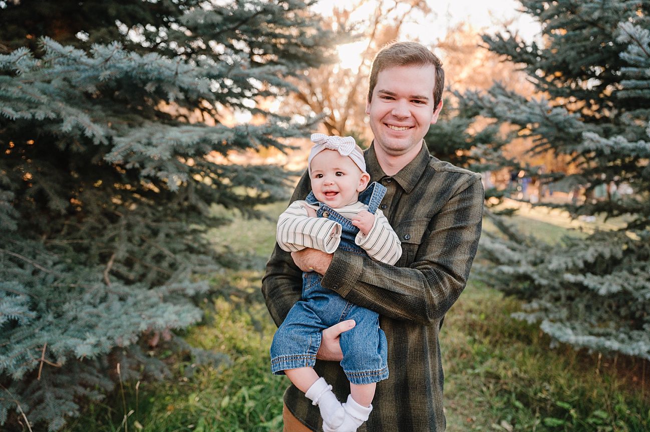 Family enjoying a playful moment together in a garden with evergreen trees at sunset.