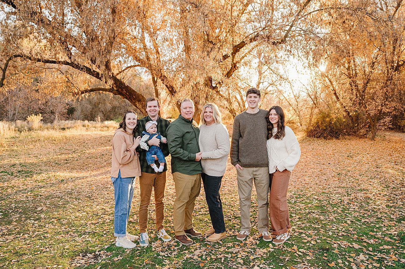 Group portrait outdoors with autumn trees and golden sunlight filtering through branches.