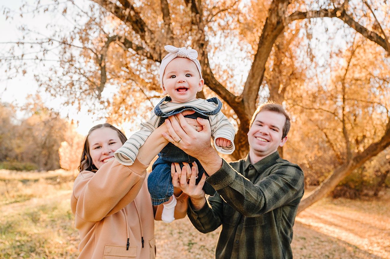 Family photo session in a park during autumn with golden leaves and warm lighting.