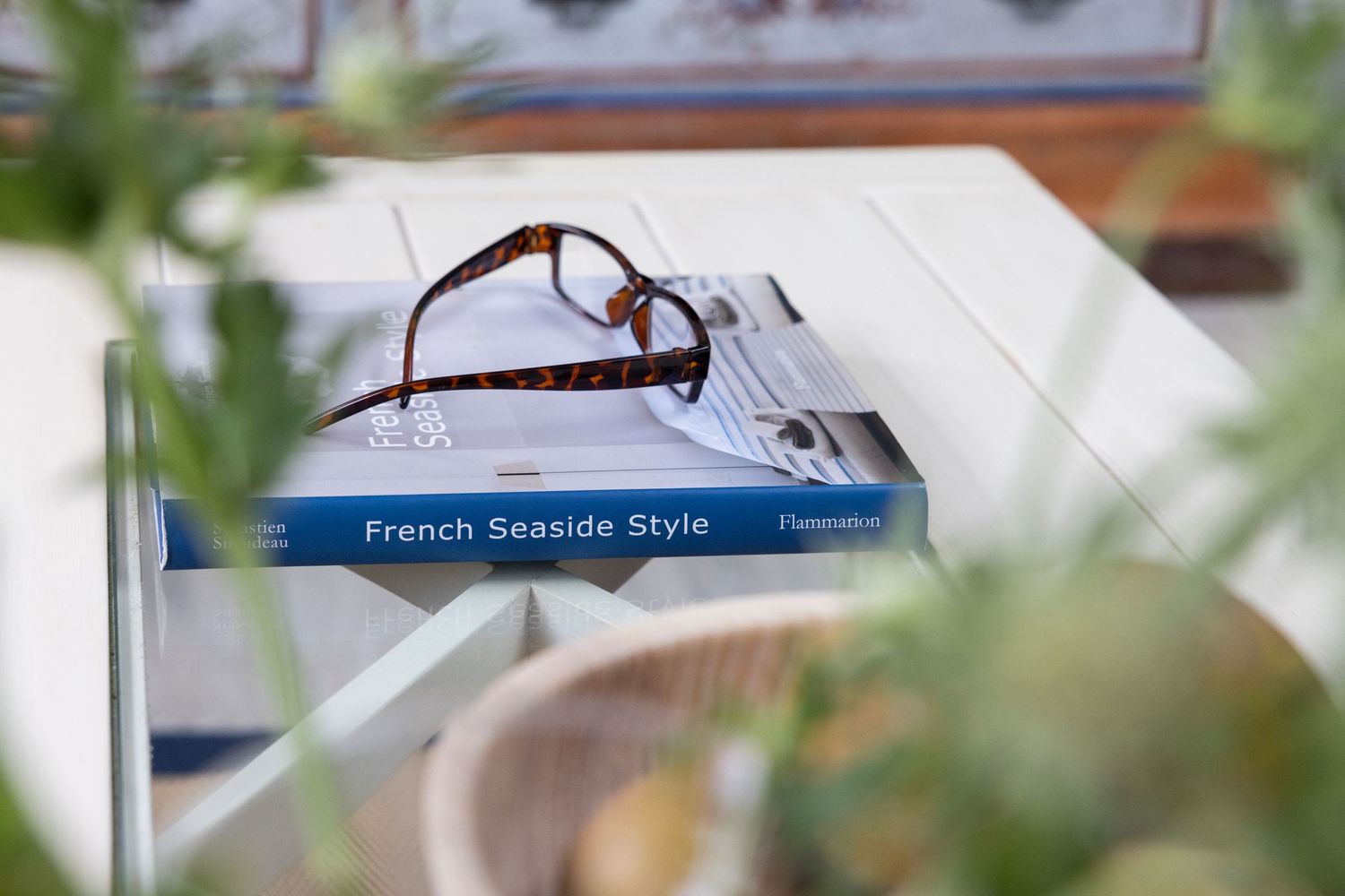 A decorative French seaside style sign hangs in a rustic outdoor setting with blurred foliage in the background.