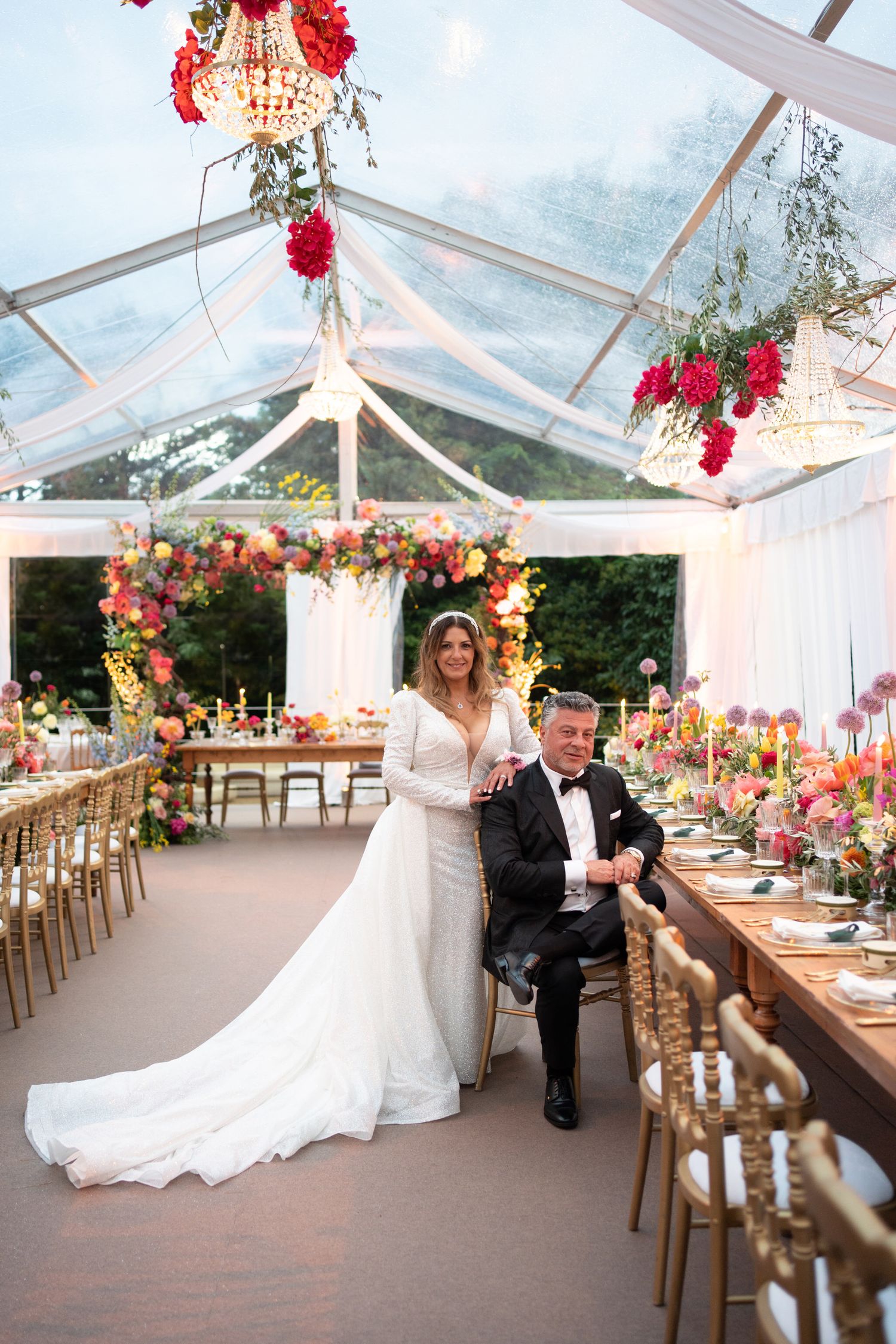 A vibrant bridal bouquet featuring pink lilies, orange tulips and yellow flowers held against a white lace dress.