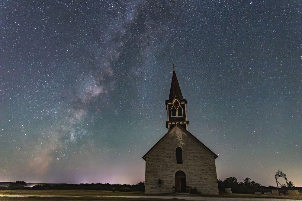 A rustic church steeple silhouetted against a starry night sky with the Milky Way galaxy visible in the background.