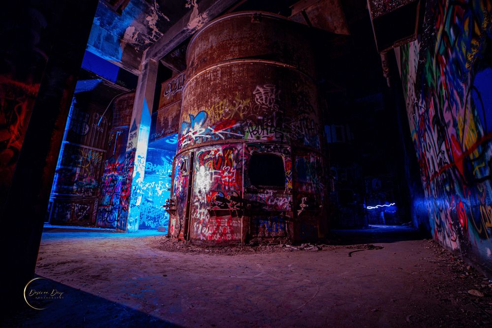 Graffiti covered industrial tank illuminated by blue light in an abandoned warehouse at night in Texas