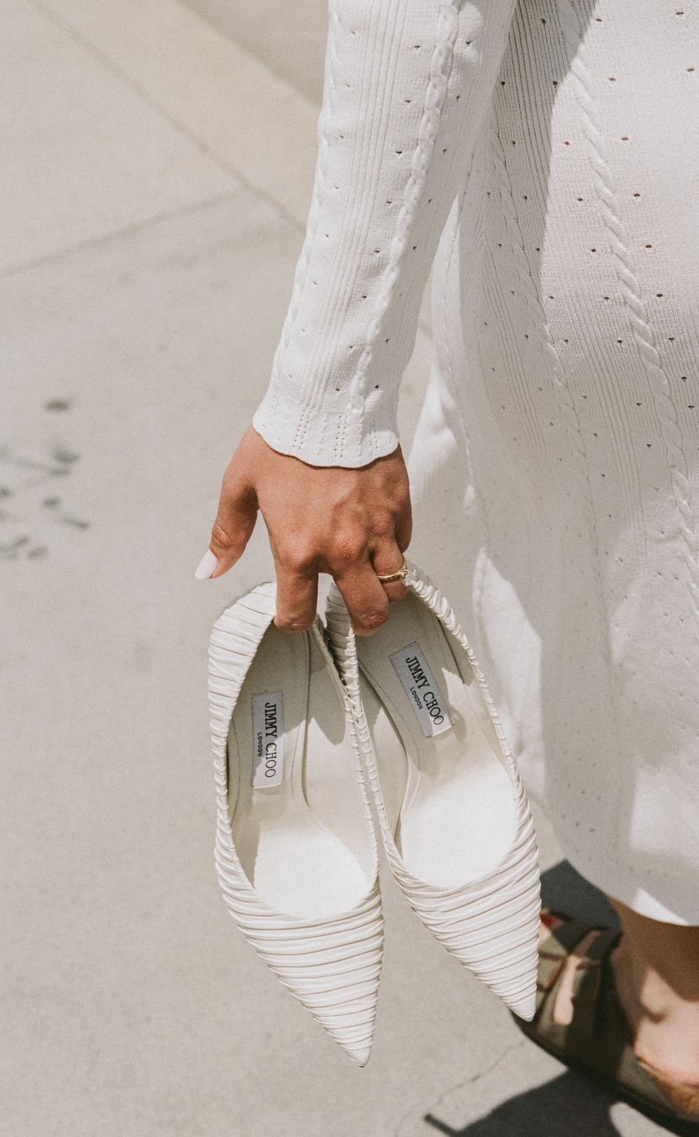 Close-up of hands holding white bridal shoes against a light-colored floor.