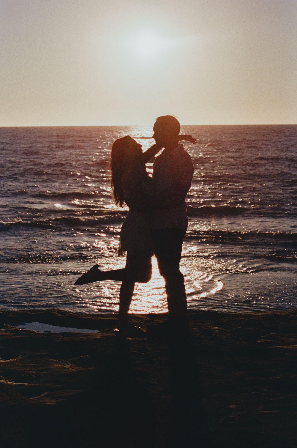 Silhouette of a couple kissing on a beach at golden sunset with shimmering ocean waves.
