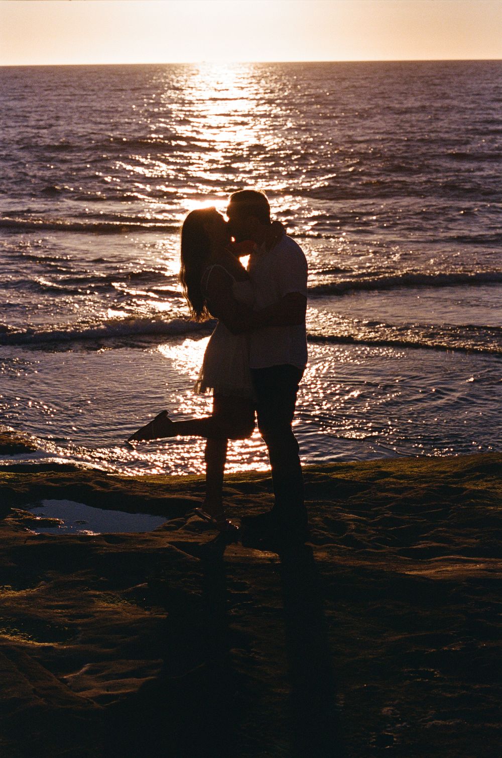 Romantic silhouette of a couple kissing on a beach during a stunning golden ocean sunset.