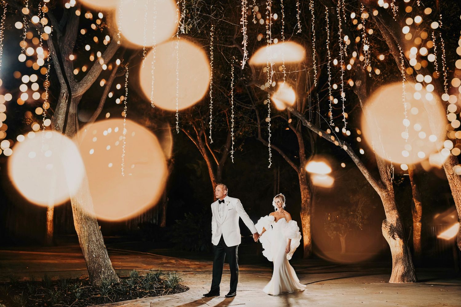 Bride and groom walking together through glowing lights at night, captured in a romantic wedding moment