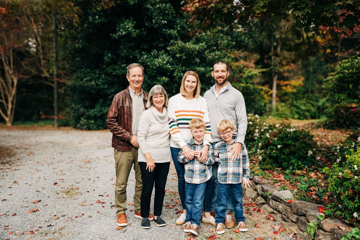 Family members smiling together on a leaf-covered path during an autumn photo session in Charlotte, NC.
