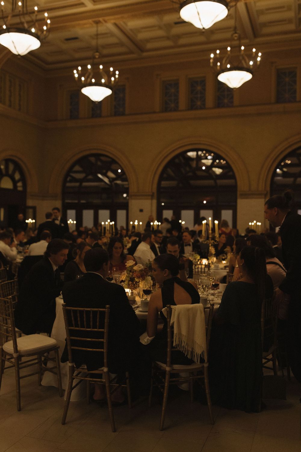 Elegant ballroom reception with chandeliers and formal table settings hosting numerous guests at round tables.