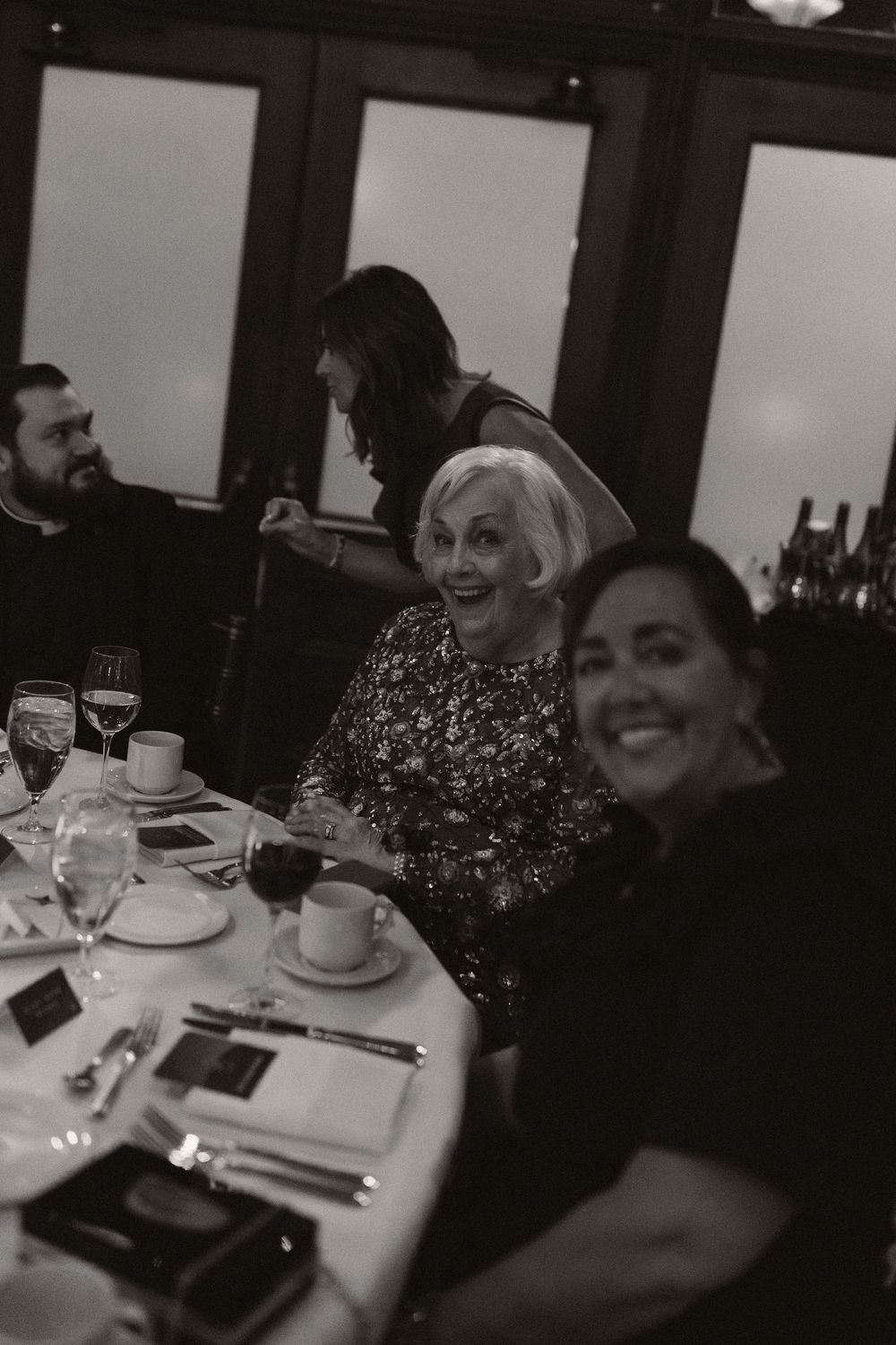 Guests enjoying conversation and drinks at an elegant dinner table setting in a dimly lit room.