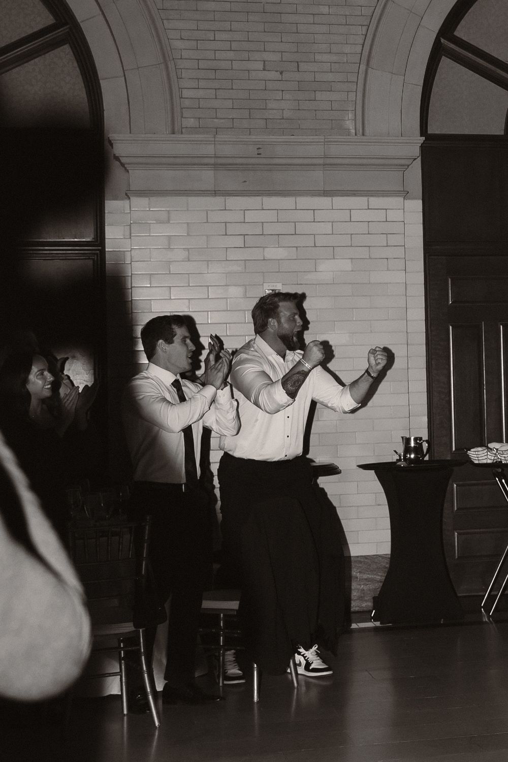 Black and white photo of guests dancing energetically in a room with white brick walls.