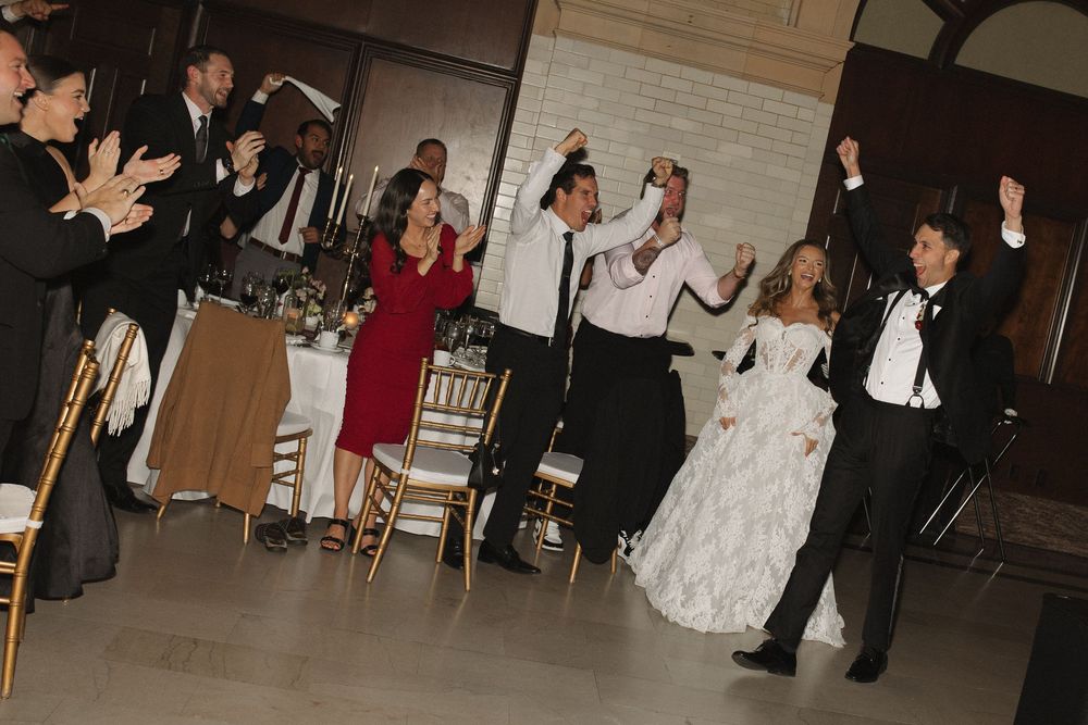 Wedding guests dance together during a reception celebration in a dimly lit banquet hall.