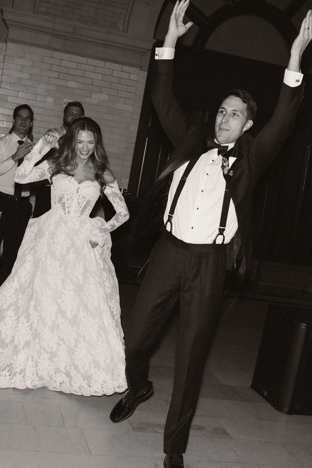 Wedding reception dance floor scene with people dancing in formal attire and a white lace dress.
