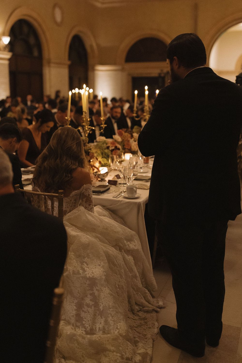 Elegant wedding reception venue with tables set with white linens and candlelight under arched ceilings.